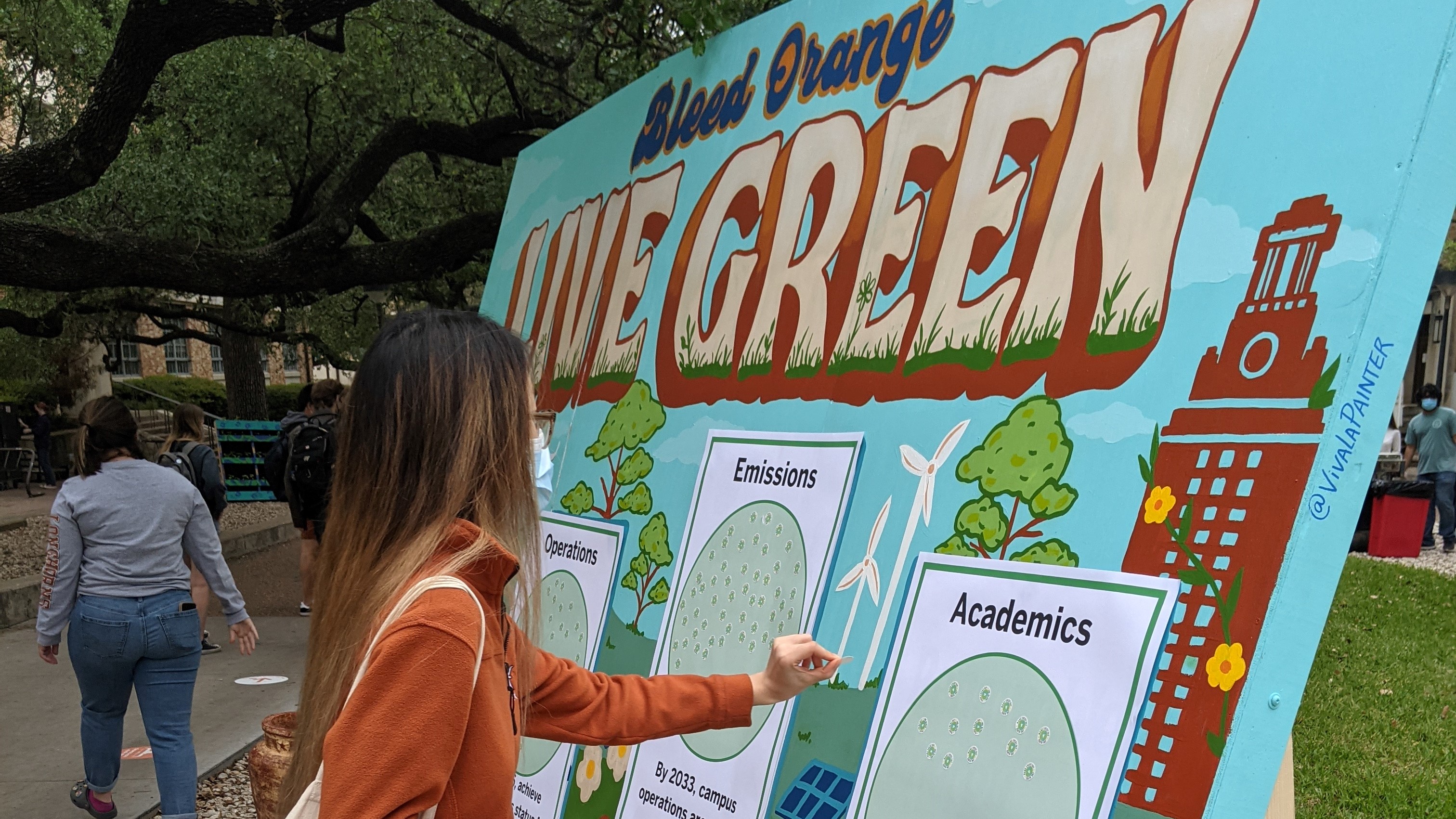 A UT student applies a sticker to a colorful mural that reads Bleed Orange Live Green.