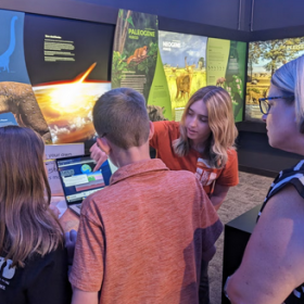 Museum staff demonstrating interactive exhibit to a family of mother, daughter, and son.