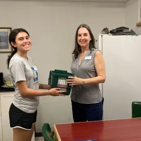 A Resource Recovery student intern hands a composting bin to a UT staff member.